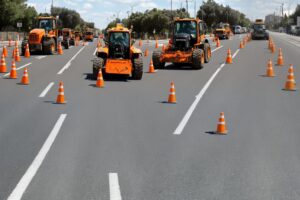 עבודות תחזוקת כביש: משאיות ומכונות כתומות עם קונוסים מסומנים